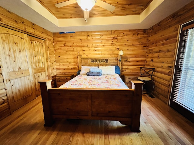bedroom featuring wood ceiling, wood-type flooring, a ceiling fan, and a tray ceiling