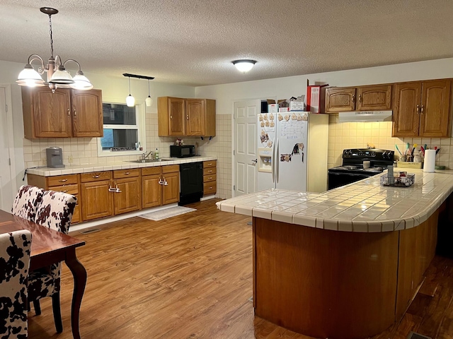 kitchen with black appliances, brown cabinetry, a sink, and wood finished floors