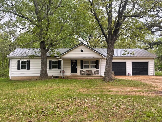 ranch-style house with a garage, dirt driveway, metal roof, and a front yard