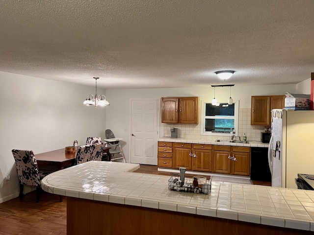 kitchen with tasteful backsplash, brown cabinets, wood finished floors, black appliances, and a sink