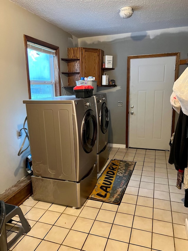 clothes washing area featuring light tile patterned floors, a textured ceiling, laundry area, baseboards, and washer and dryer