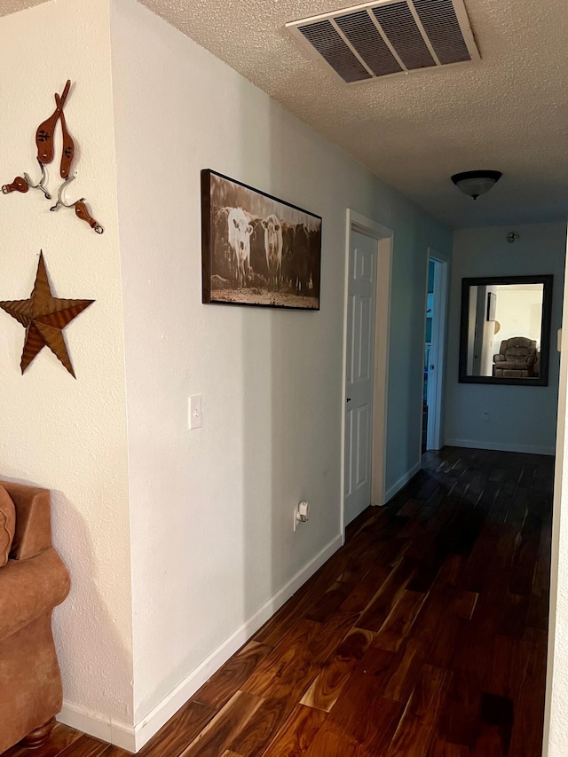 hall featuring visible vents, dark wood finished floors, a textured ceiling, and baseboards