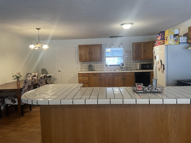 kitchen with backsplash, tile countertops, black appliances, and an inviting chandelier