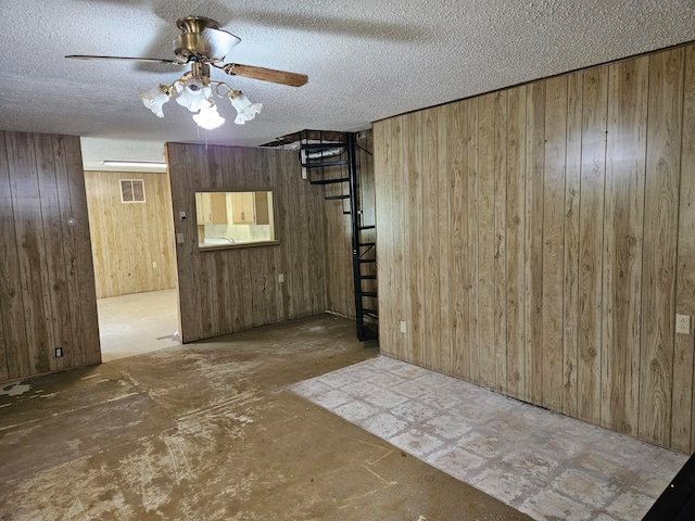 spare room with ceiling fan, a textured ceiling, and wood walls