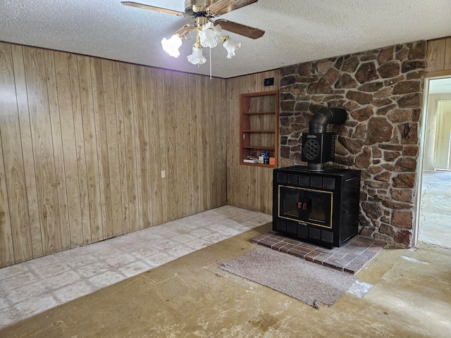 unfurnished living room with a textured ceiling, wooden walls, and a wood stove