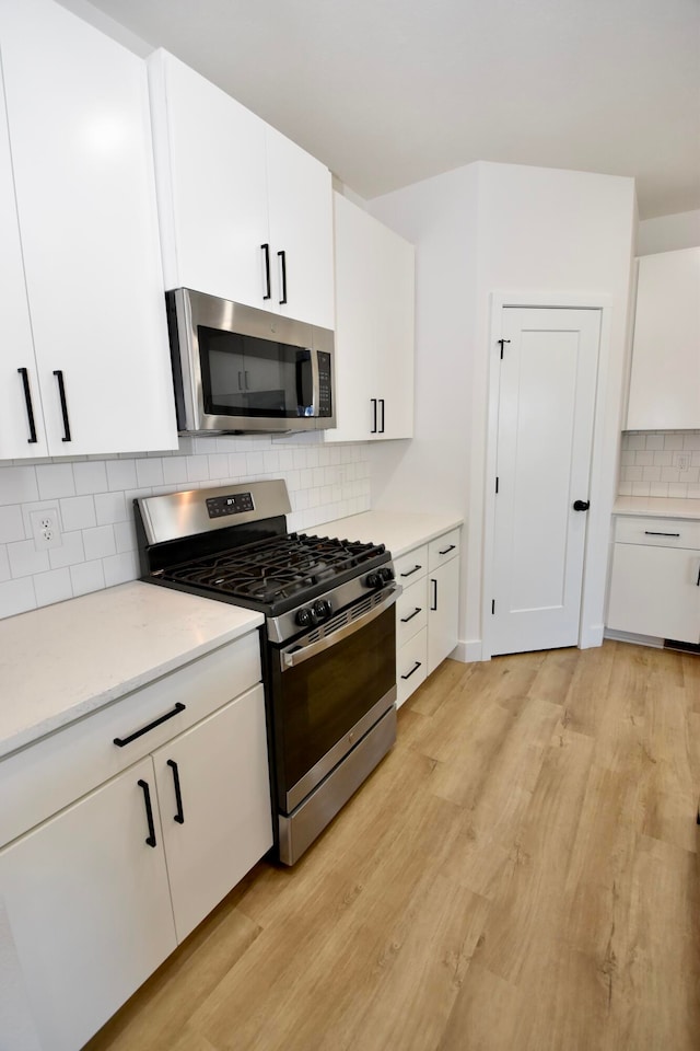 kitchen with stainless steel appliances, backsplash, light hardwood / wood-style flooring, and white cabinetry