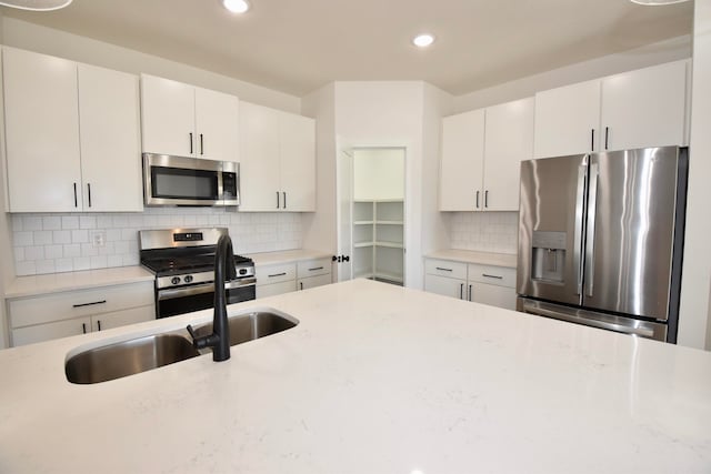 kitchen featuring light stone counters, white cabinetry, stainless steel appliances, and backsplash