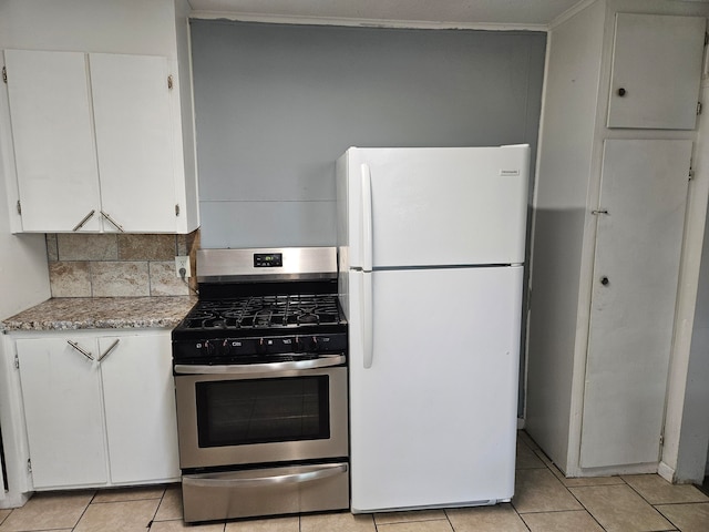 kitchen featuring white refrigerator, light tile patterned flooring, stainless steel gas range, backsplash, and white cabinets