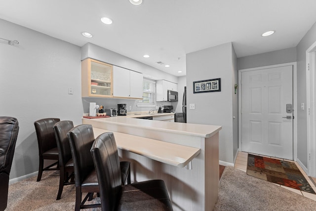 kitchen featuring black appliances, white cabinets, kitchen peninsula, a kitchen bar, and light colored carpet