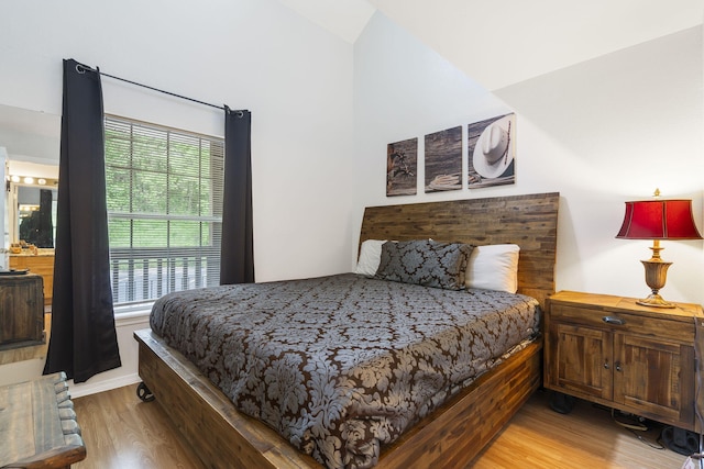 bedroom with light wood-type flooring, lofted ceiling, and connected bathroom