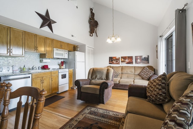 kitchen featuring white appliances, decorative light fixtures, a chandelier, high vaulted ceiling, and light hardwood / wood-style floors