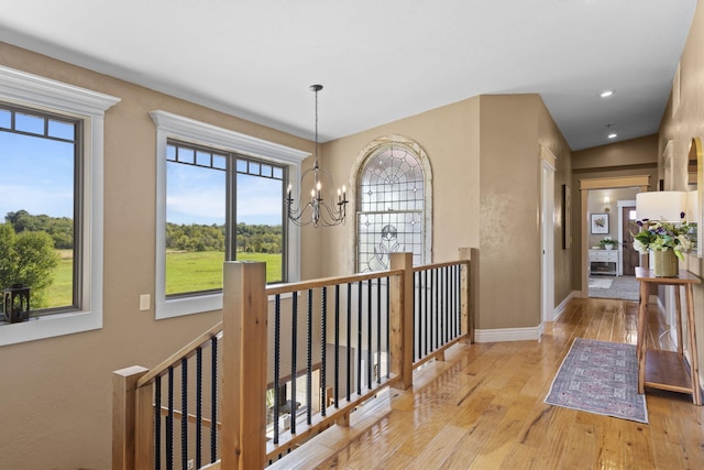 corridor with light hardwood / wood-style floors, an inviting chandelier, and a wealth of natural light