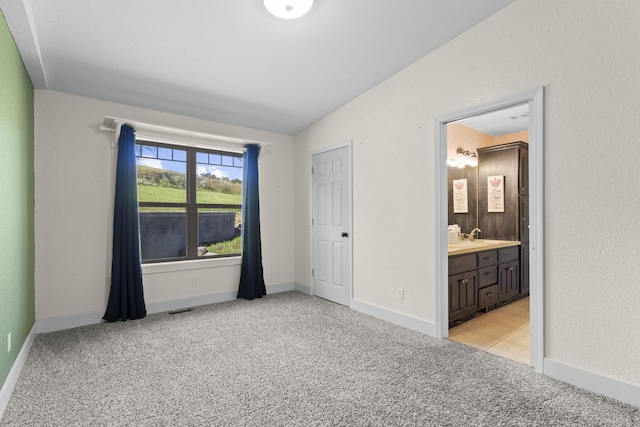 unfurnished bedroom featuring lofted ceiling, light colored carpet, and ensuite bath