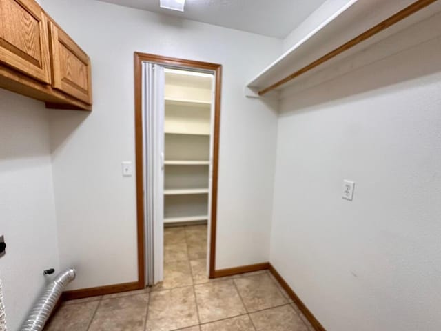 clothes washing area featuring hookup for an electric dryer, cabinet space, light tile patterned flooring, and baseboards