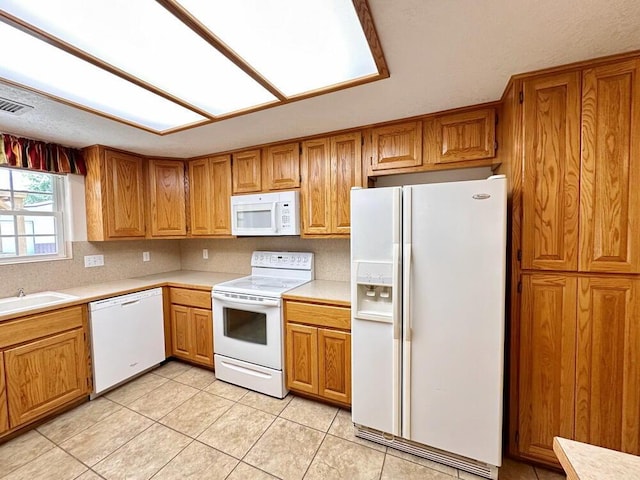 kitchen featuring brown cabinets, a sink, white appliances, and light countertops