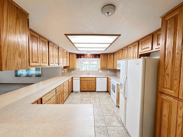 kitchen featuring light tile patterned floors, kitchen peninsula, sink, white appliances, and a textured ceiling