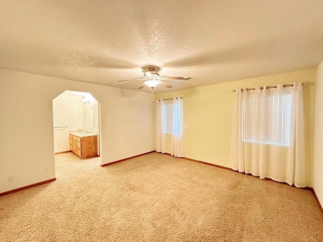 spare room with arched walkways, a textured ceiling, a ceiling fan, and baseboards
