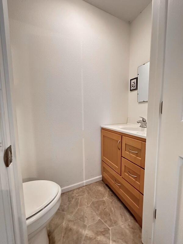 half bath with baseboards, vanity, and toilet