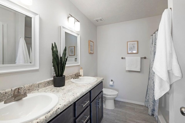 bathroom with a textured ceiling, hardwood / wood-style floors, vanity, and toilet