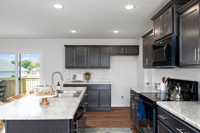 kitchen with black appliances, a kitchen island with sink, sink, dark hardwood / wood-style flooring, and a textured ceiling