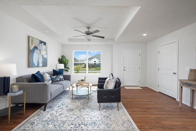 living room featuring dark wood-type flooring, a raised ceiling, a textured ceiling, and ceiling fan