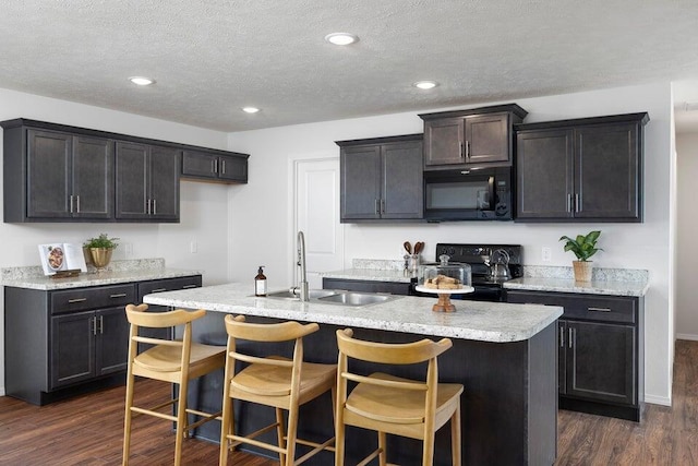 kitchen featuring sink, a textured ceiling, a center island with sink, black appliances, and dark hardwood / wood-style flooring