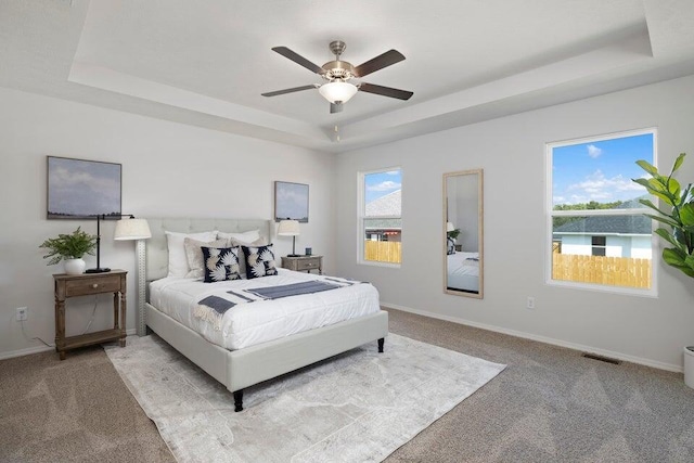 carpeted bedroom featuring a raised ceiling, multiple windows, and ceiling fan