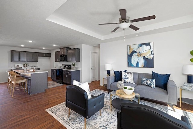 living room with a raised ceiling, dark hardwood / wood-style floors, sink, and ceiling fan