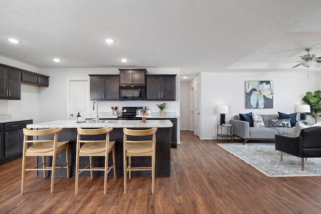 kitchen with dark brown cabinetry, a center island with sink, dark hardwood / wood-style flooring, and black appliances