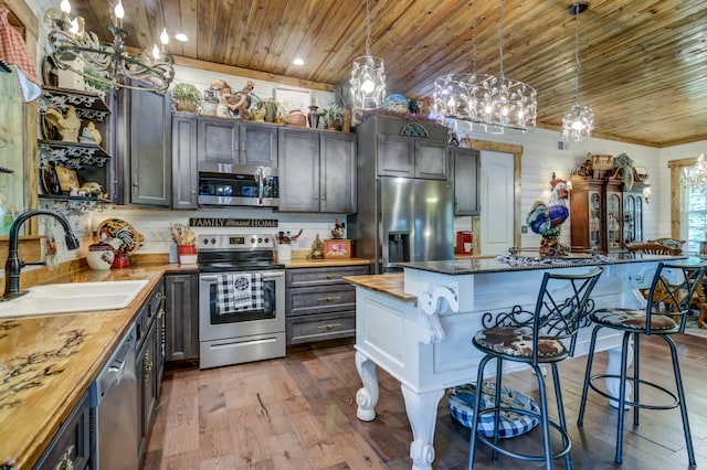 kitchen with sink, decorative light fixtures, stainless steel appliances, a breakfast bar area, and wood counters