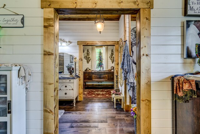 interior space with dark wood-type flooring, wood walls, and beamed ceiling