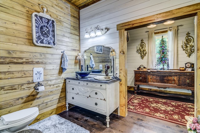 bathroom with wood-type flooring, vanity, wooden walls, and toilet