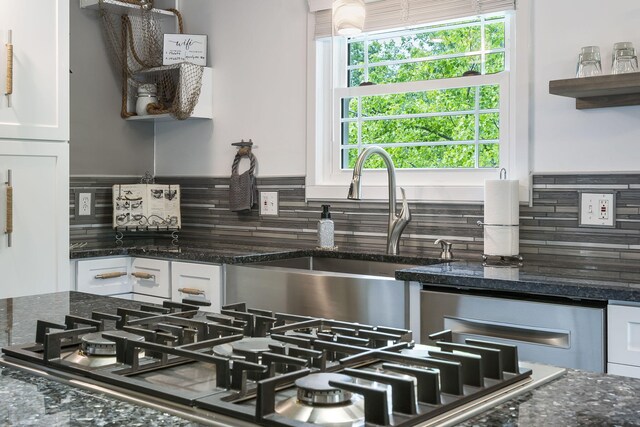 room details featuring white cabinets, decorative backsplash, dark stone countertops, and sink