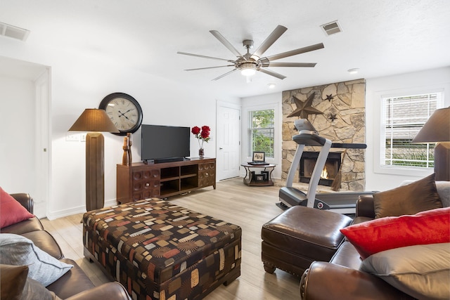 living room featuring ceiling fan, light hardwood / wood-style floors, and a stone fireplace