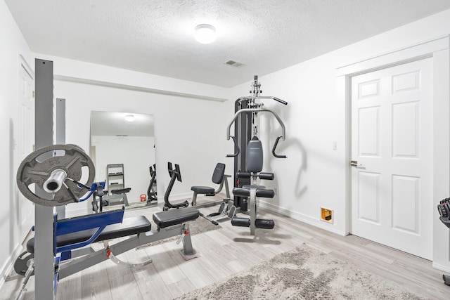 workout room with a textured ceiling and light wood-type flooring