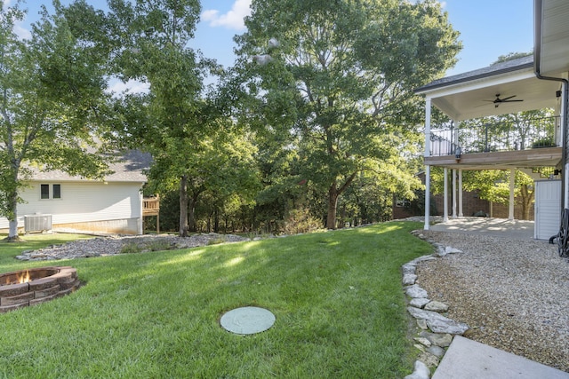 view of yard with central AC unit, ceiling fan, a deck, and an outdoor fire pit