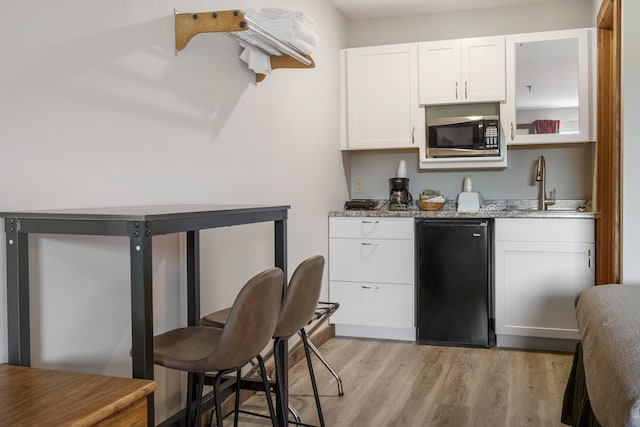 kitchen with light stone countertops, black appliances, light hardwood / wood-style flooring, and white cabinetry