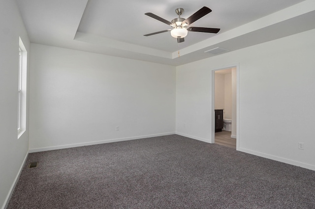 carpeted empty room featuring ceiling fan and a raised ceiling