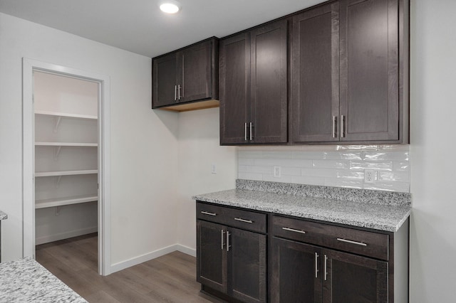 kitchen featuring dark brown cabinets, light stone counters, decorative backsplash, and dark hardwood / wood-style floors