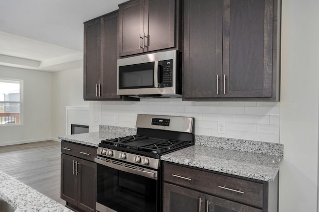 kitchen featuring light wood-type flooring, light stone countertops, dark brown cabinetry, and stainless steel appliances