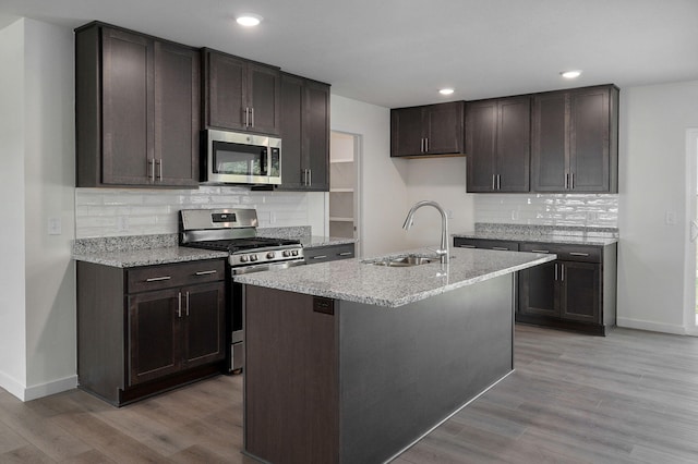 kitchen with an island with sink, sink, stainless steel appliances, and light hardwood / wood-style flooring