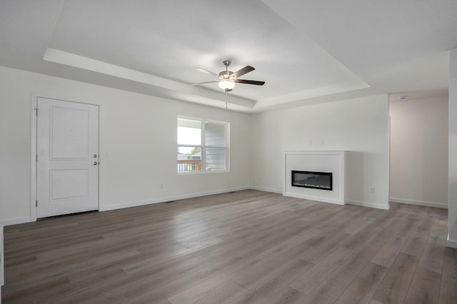 unfurnished living room with a raised ceiling, hardwood / wood-style floors, and ceiling fan