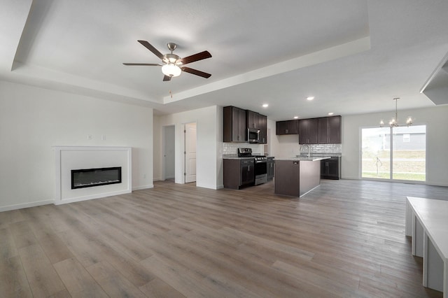 unfurnished living room featuring ceiling fan with notable chandelier, a raised ceiling, sink, and light hardwood / wood-style flooring