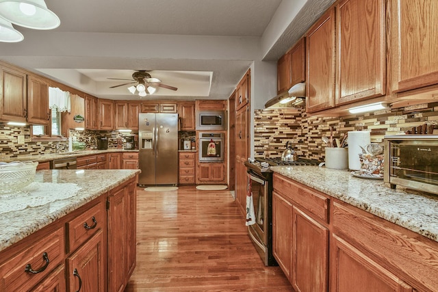 kitchen with light wood finished floors, backsplash, ceiling fan, under cabinet range hood, and appliances with stainless steel finishes