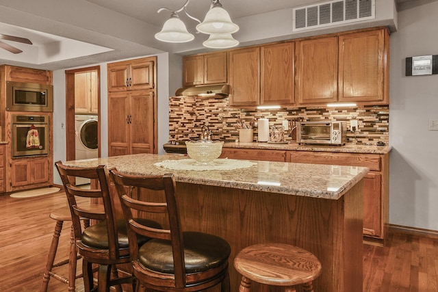kitchen with wood finished floors, appliances with stainless steel finishes, washer / clothes dryer, under cabinet range hood, and visible vents