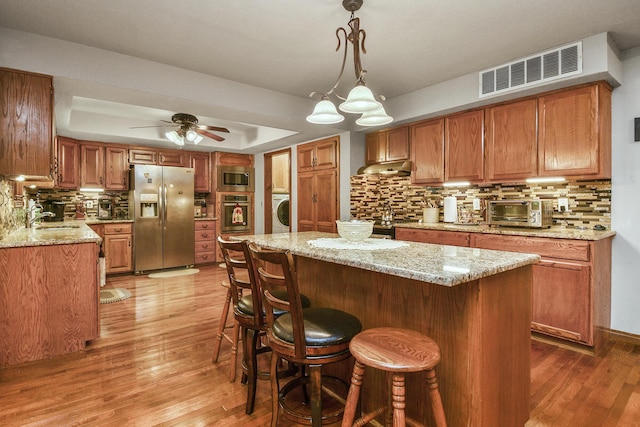 kitchen featuring visible vents, brown cabinets, appliances with stainless steel finishes, and washer / clothes dryer
