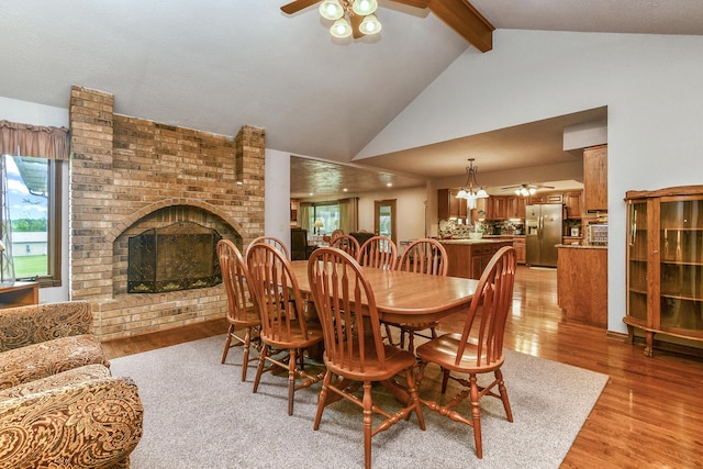 dining area featuring light wood-style flooring, a brick fireplace, beam ceiling, and ceiling fan