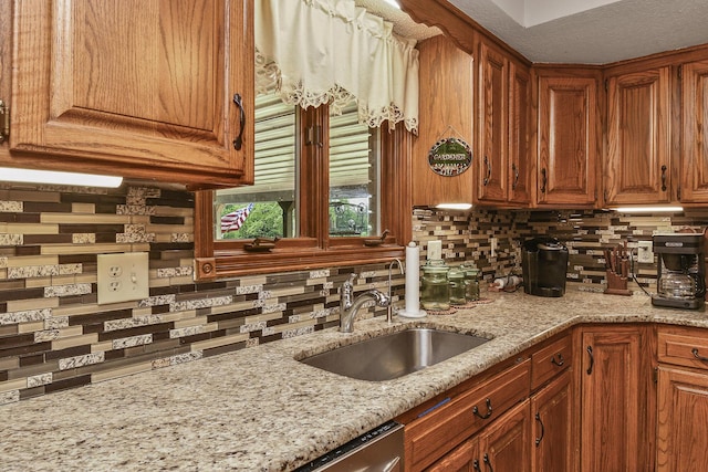 kitchen with brown cabinetry, backsplash, light stone counters, and a sink