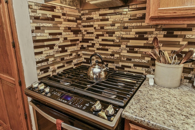 interior details with light stone countertops, decorative backsplash, and stainless steel gas range