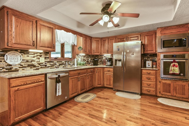 kitchen featuring a sink, light wood-type flooring, brown cabinets, ceiling fan, and appliances with stainless steel finishes